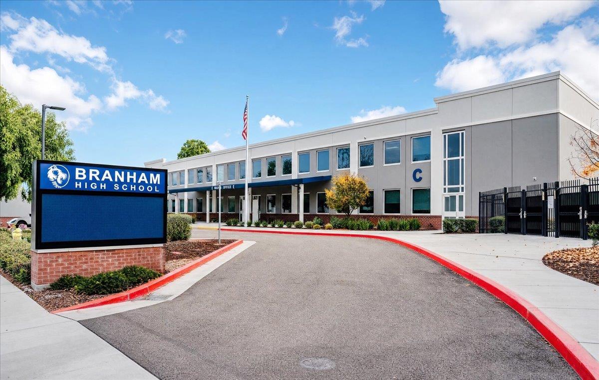 Branham High School exterior with its blue sign, flagpole, and gated entrance.