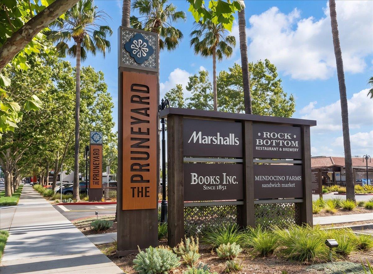 The Pruneyard shopping center sign beside a palm-lined walkway, with tenant directory panels.