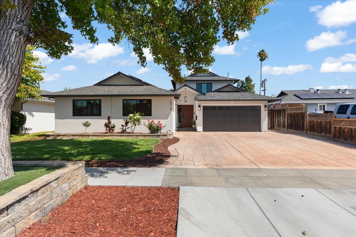 Home exterior with an attached garage, wide paved driveway, landscaped lawn, and mature shade tree.