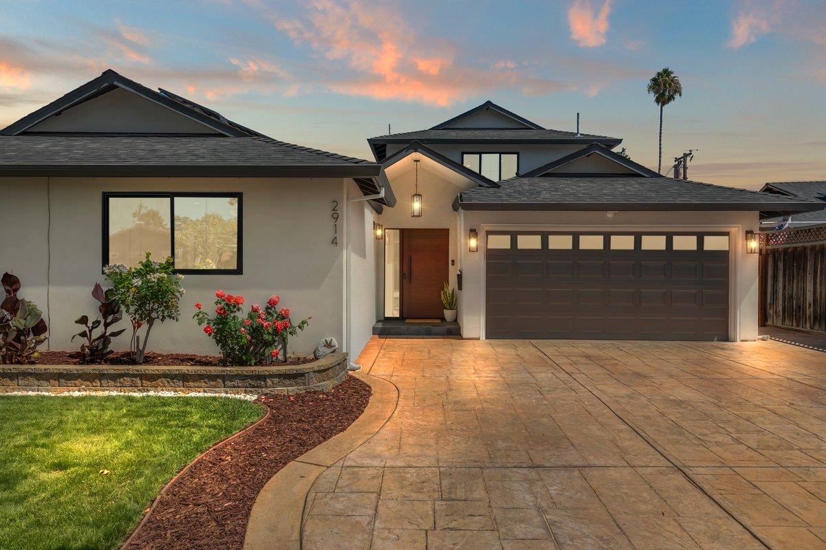 Modern home with a dark double garage, stamped driveway, and landscaped garden at dusk.