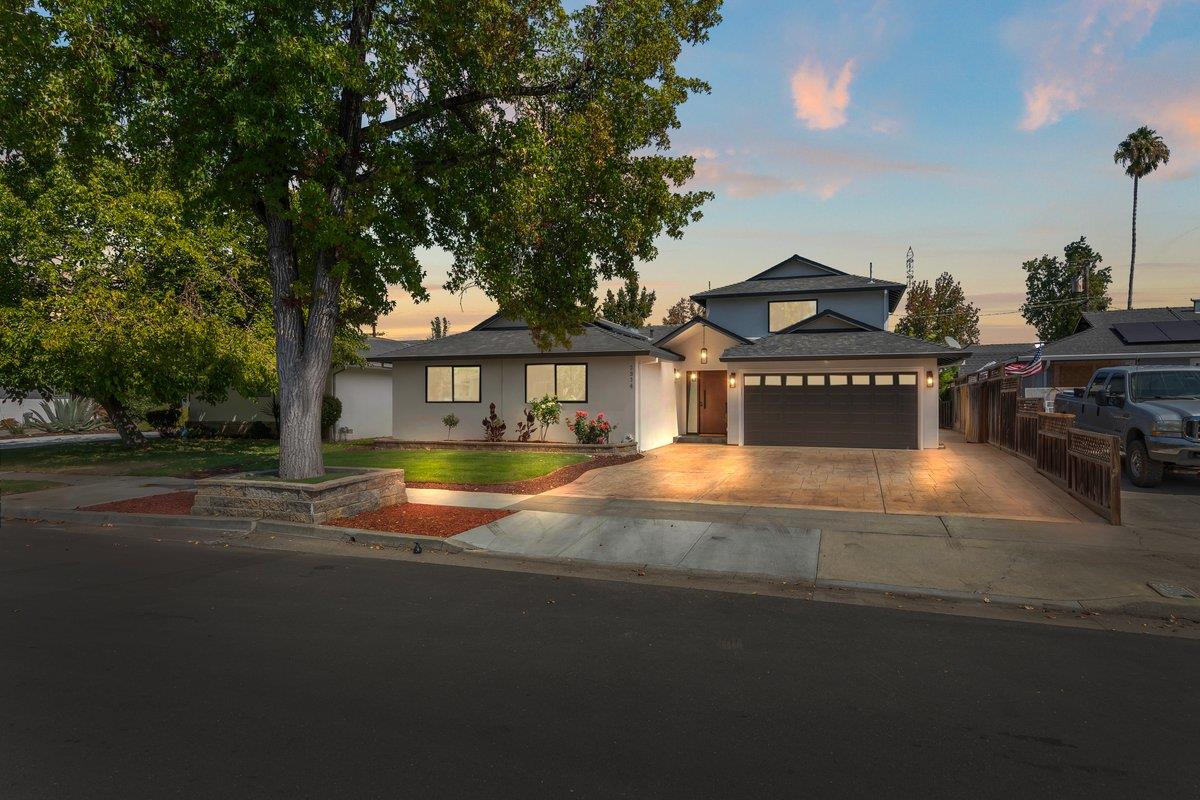 Home exterior with a two-car garage, wide driveway, and large shade tree at dusk.