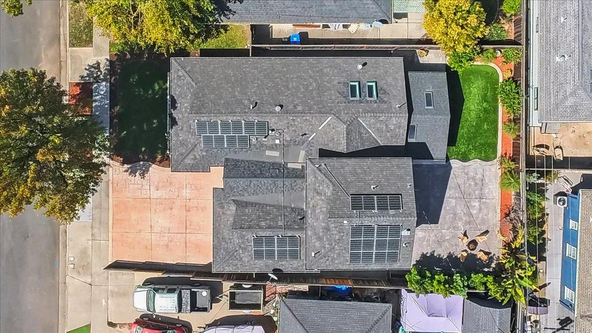 Aerial view of a home with multiple solar panel arrays across its roof and a driveway alongside.