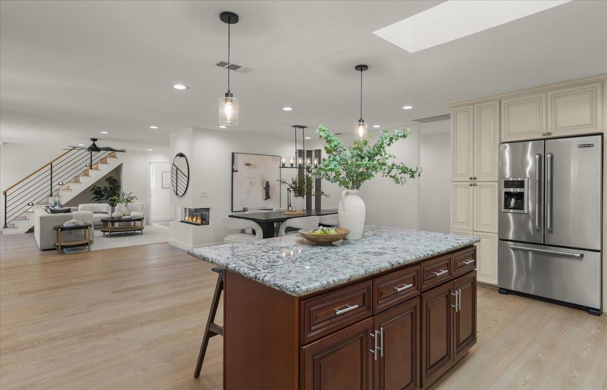 Open-plan kitchen with a large stone-topped island, cream cabinets, and living area beside a staircase.