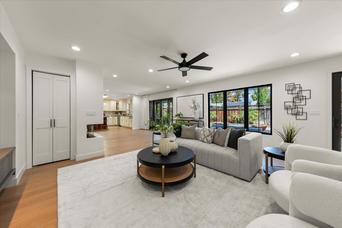 Staged living room with gray sectional, black-framed garden windows, and an open kitchen.