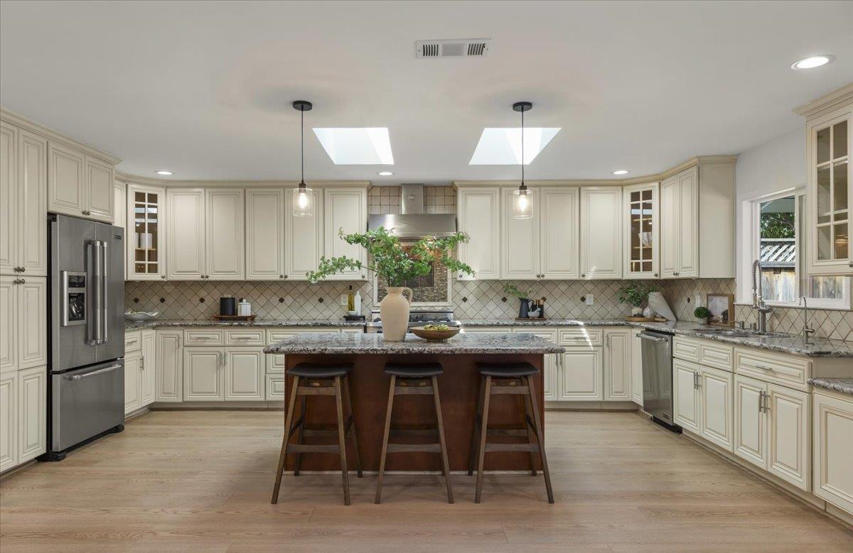 Spacious cream kitchen with a central island, three stools, stainless steel appliances, and two skylights.