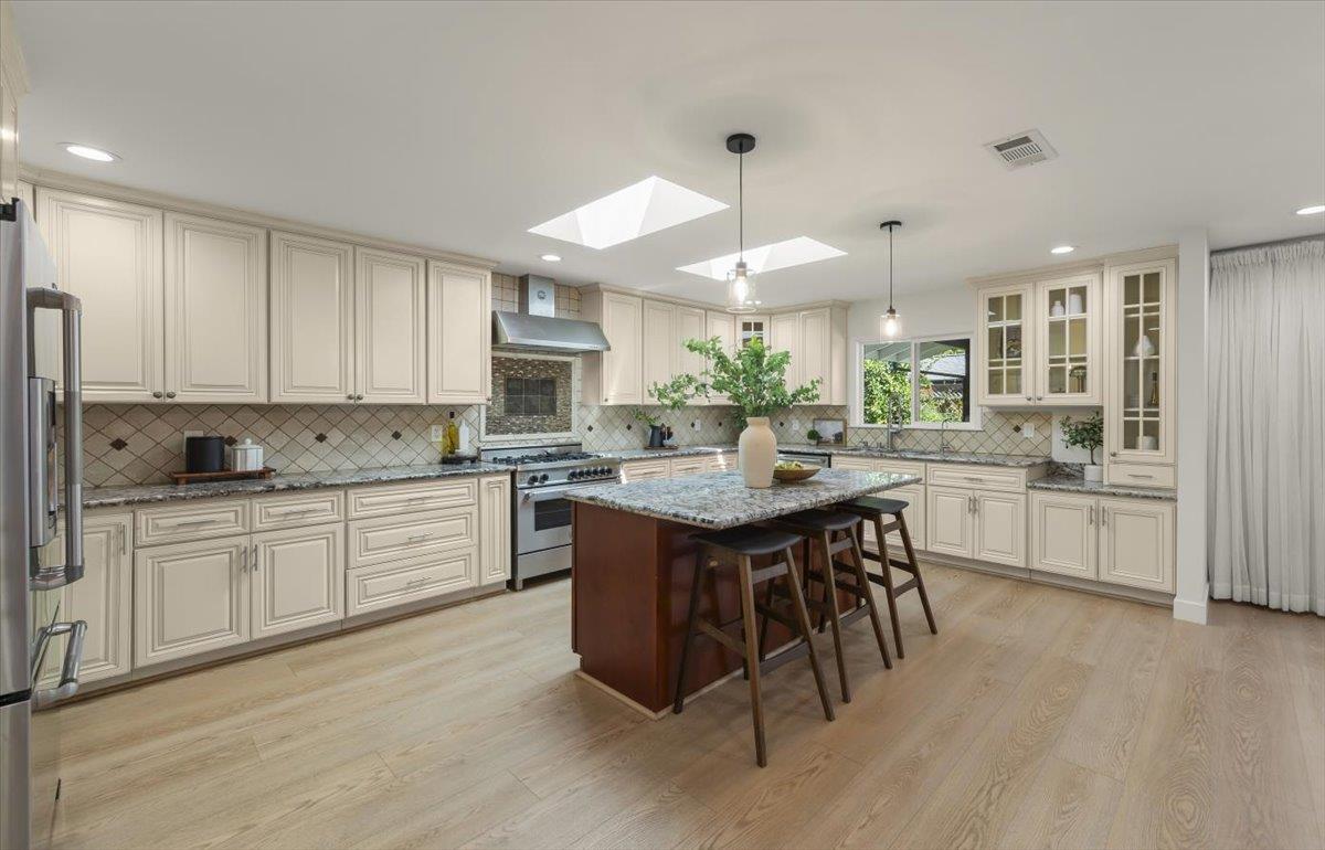 Kitchen with cream cabinetry, granite counters, and a dark wood island beneath skylights.