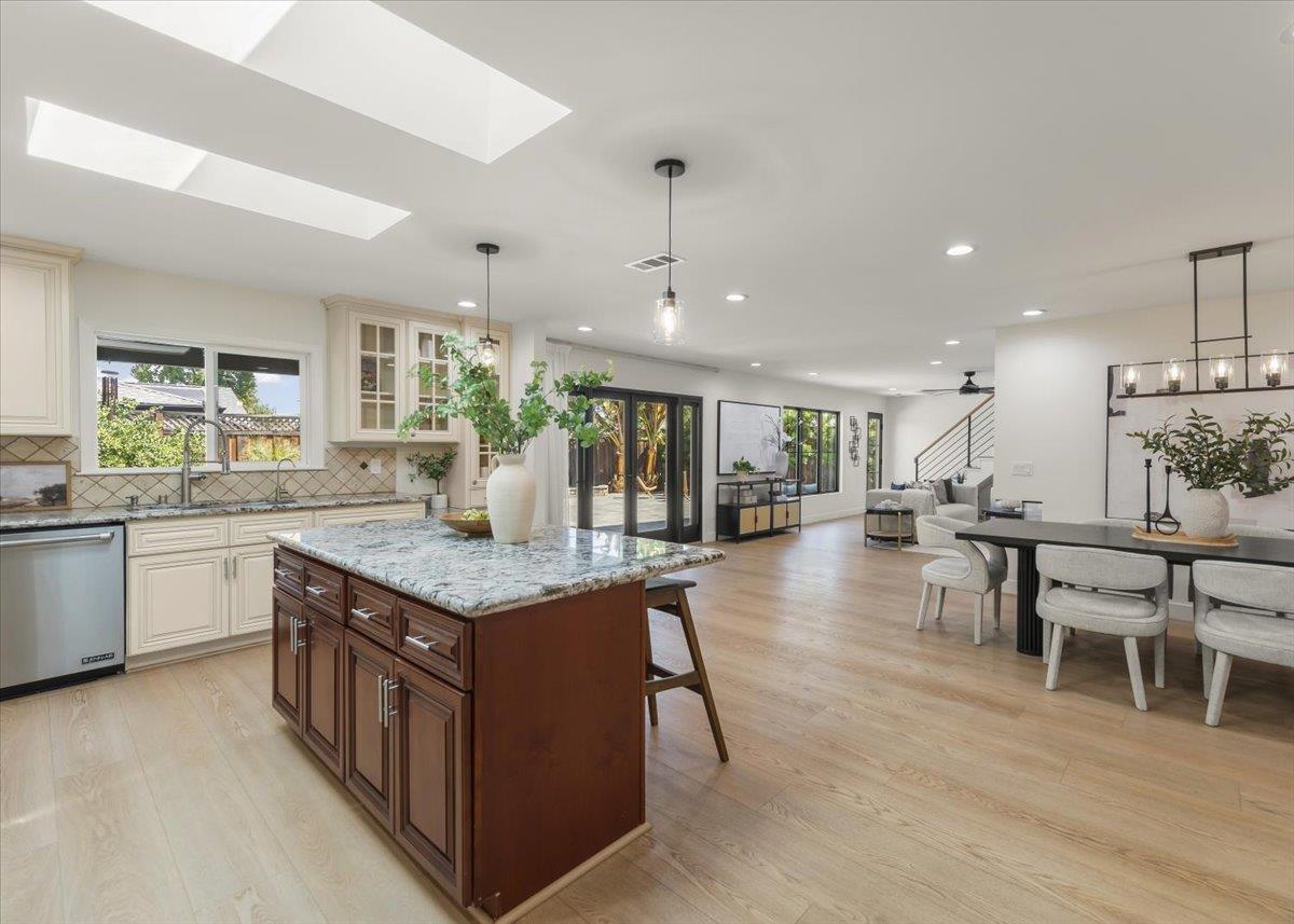 Open-plan kitchen with a dark wood island, patterned stone countertop, skylights, and sliding glass doors.