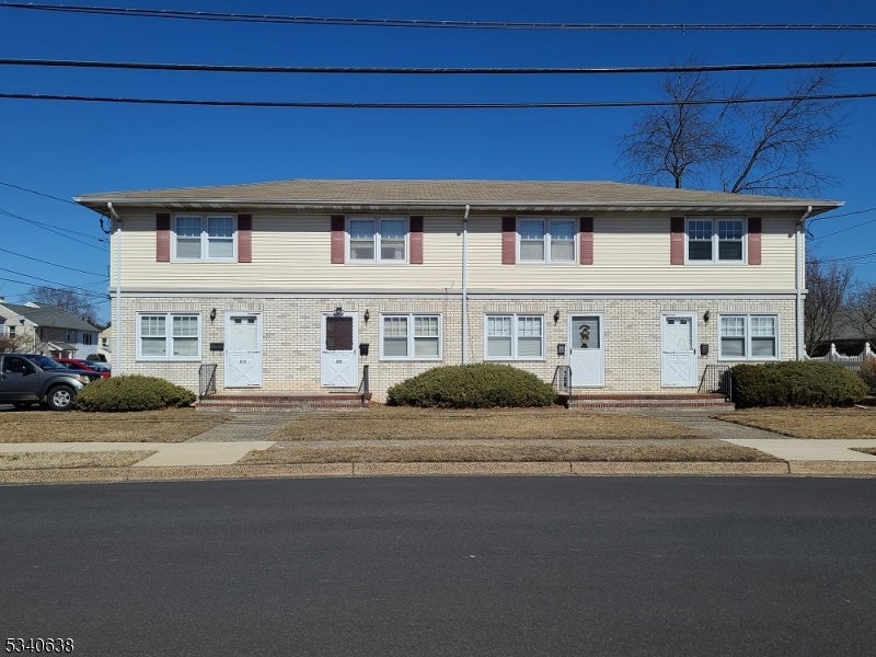 Two-story multi-unit building with light brick, red shutters, and several separate entrances.
