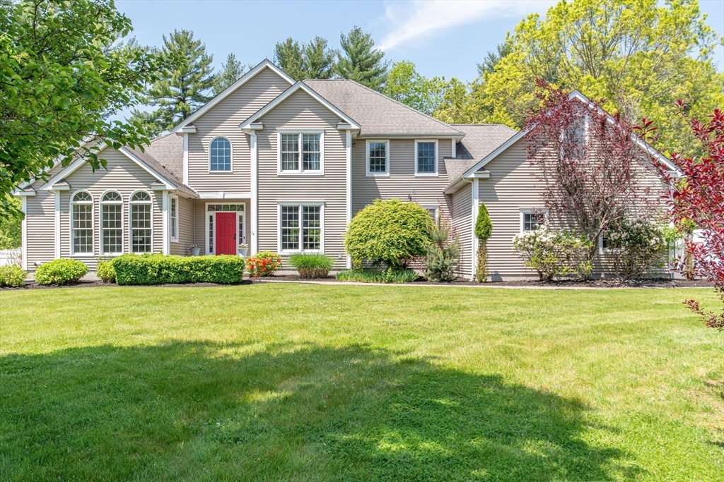 Two-story beige home with a red front door, arched windows, and a broad green lawn.