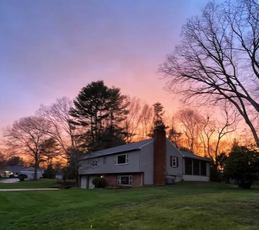 Gray split-level home with a brick chimney and broad lawn at dusk.
