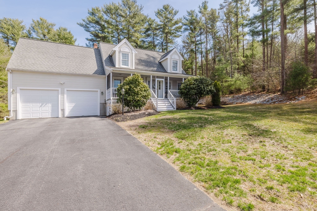 Light-colored two-story home with a covered porch, two-car garage, and wooded surroundings.