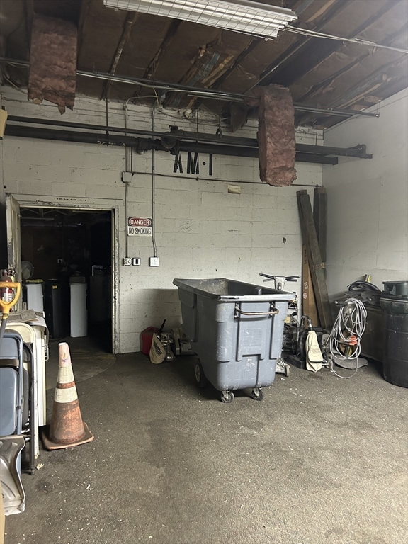 Garage with concrete-block walls, exposed ceiling, and a large rolling waste bin.