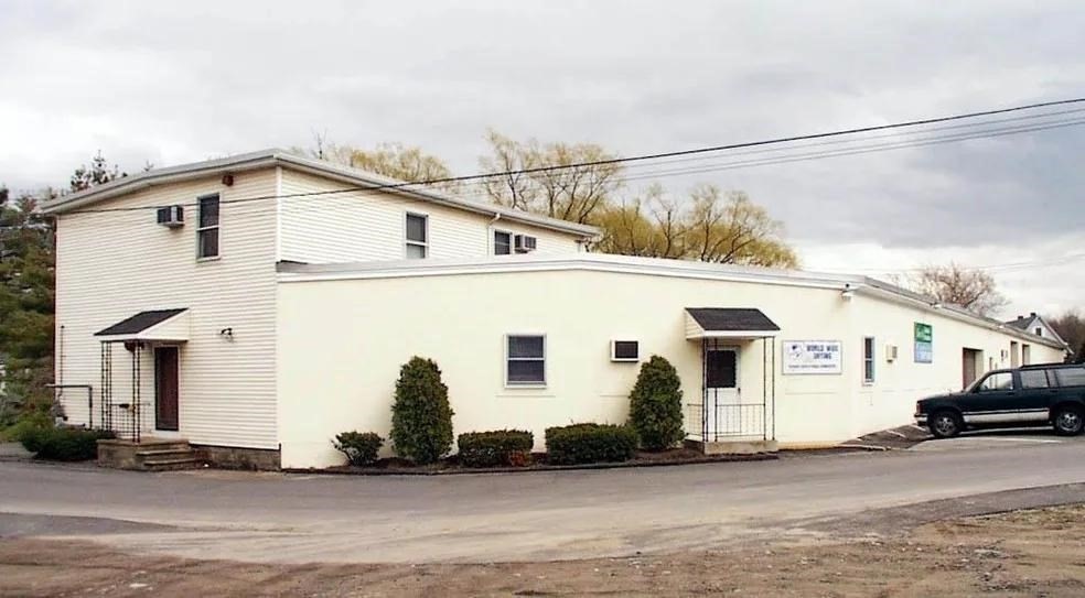 White commercial building with a two-story section, two awning-covered entrances, and shrubs along the front.
