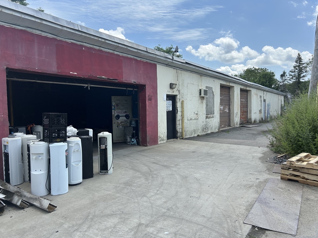 Weathered industrial building with an open garage bay, several doors, and a broad concrete driveway.