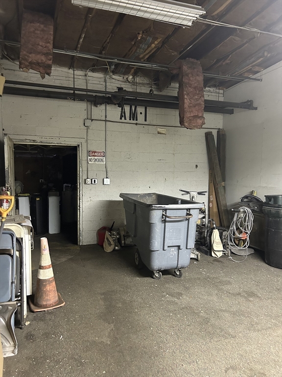 Garage utility area with exposed beams, a wheeled tub, traffic cone, and equipment storage.