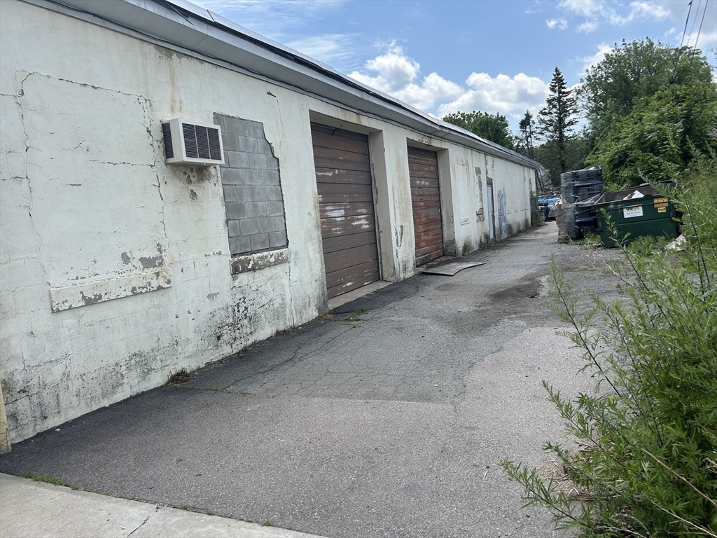 Weathered industrial building with several roll-up doors beside an asphalt service lane.
