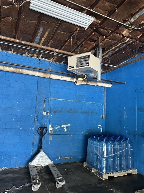 Blue commercial storage room with exposed ceiling insulation, a pallet jack, and bottled water on pallets.