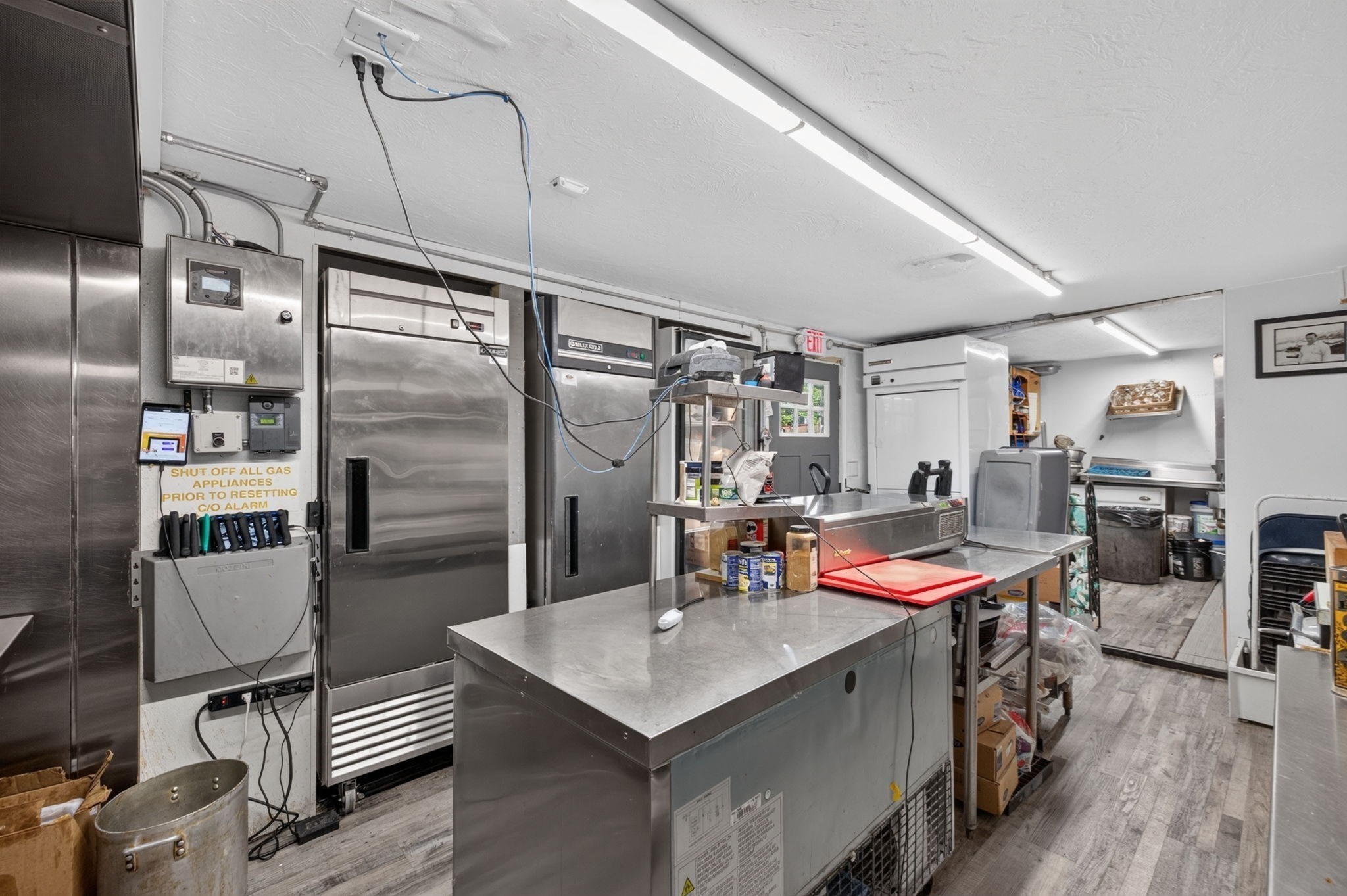 Commercial kitchen with stainless-steel worktables and large refrigerators.