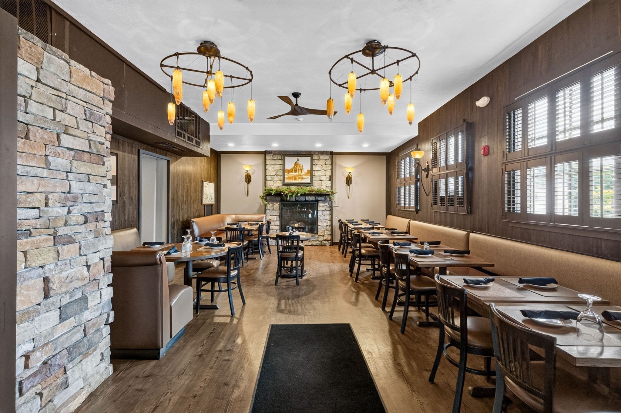 Restaurant dining room with set tables, shuttered windows, and a stone fireplace.