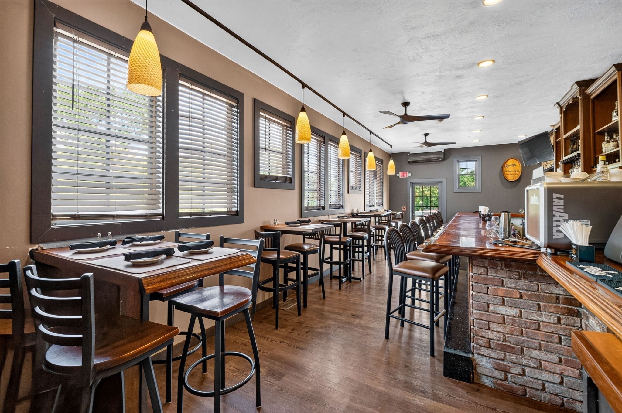 Restaurant dining room with window-side tables and a long brick-front bar.