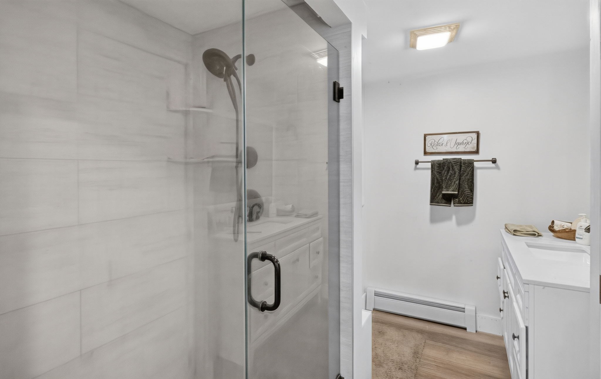 Bathroom with a glass shower, white tile, dark fixtures, and a white vanity.