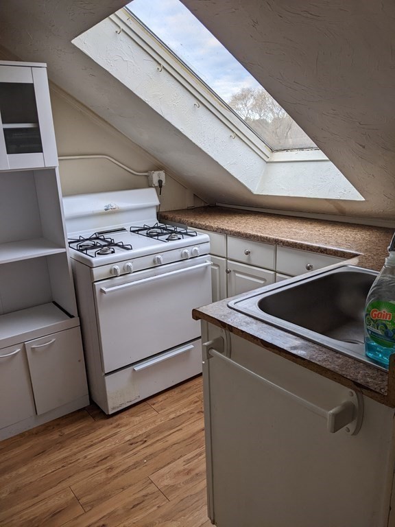 Kitchen with a large sloped skylight, white cabinets, gas range, and brown countertops.