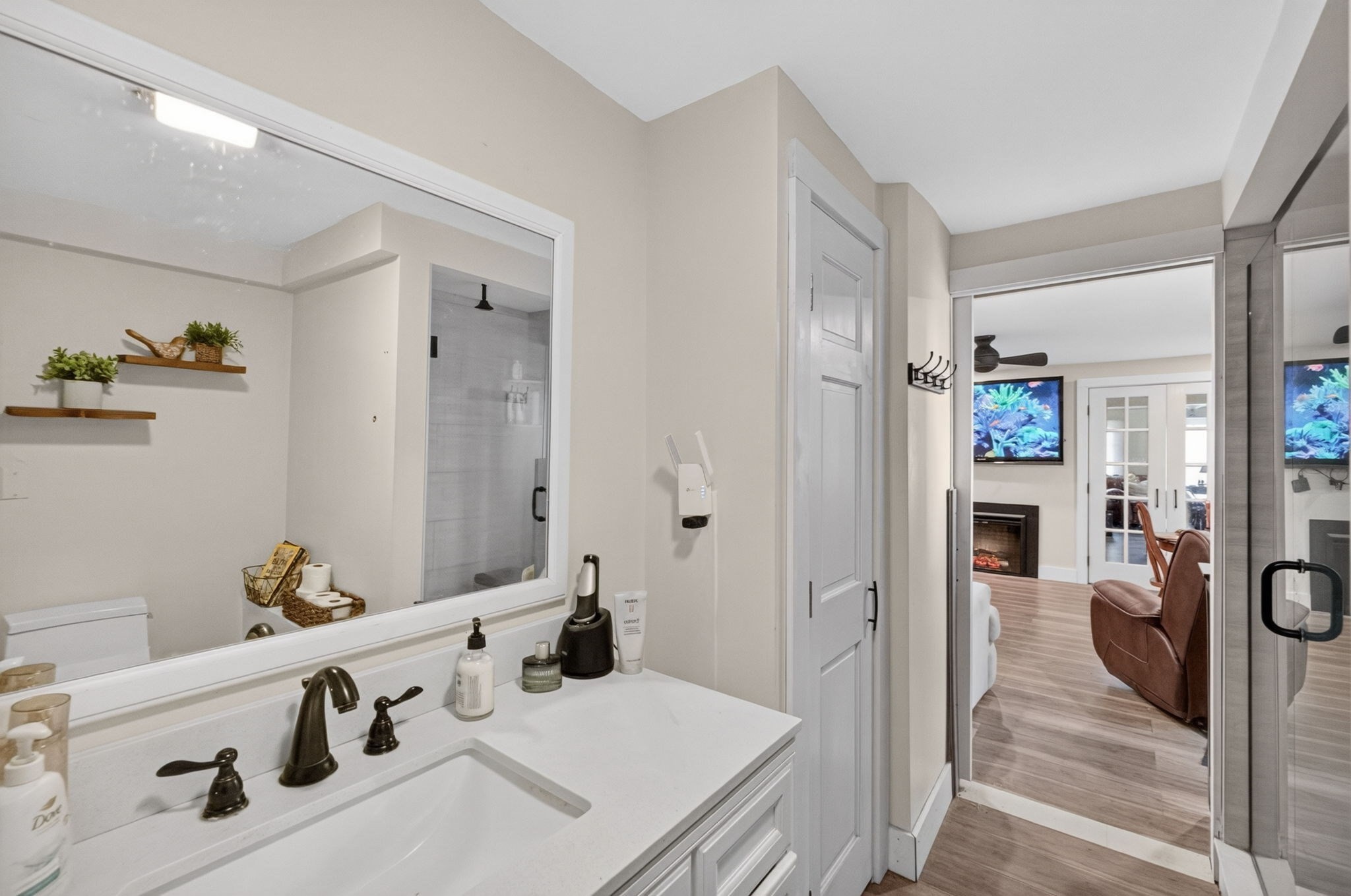 Bathroom vanity and glass shower, with a view through the doorway to a living room and fireplace.