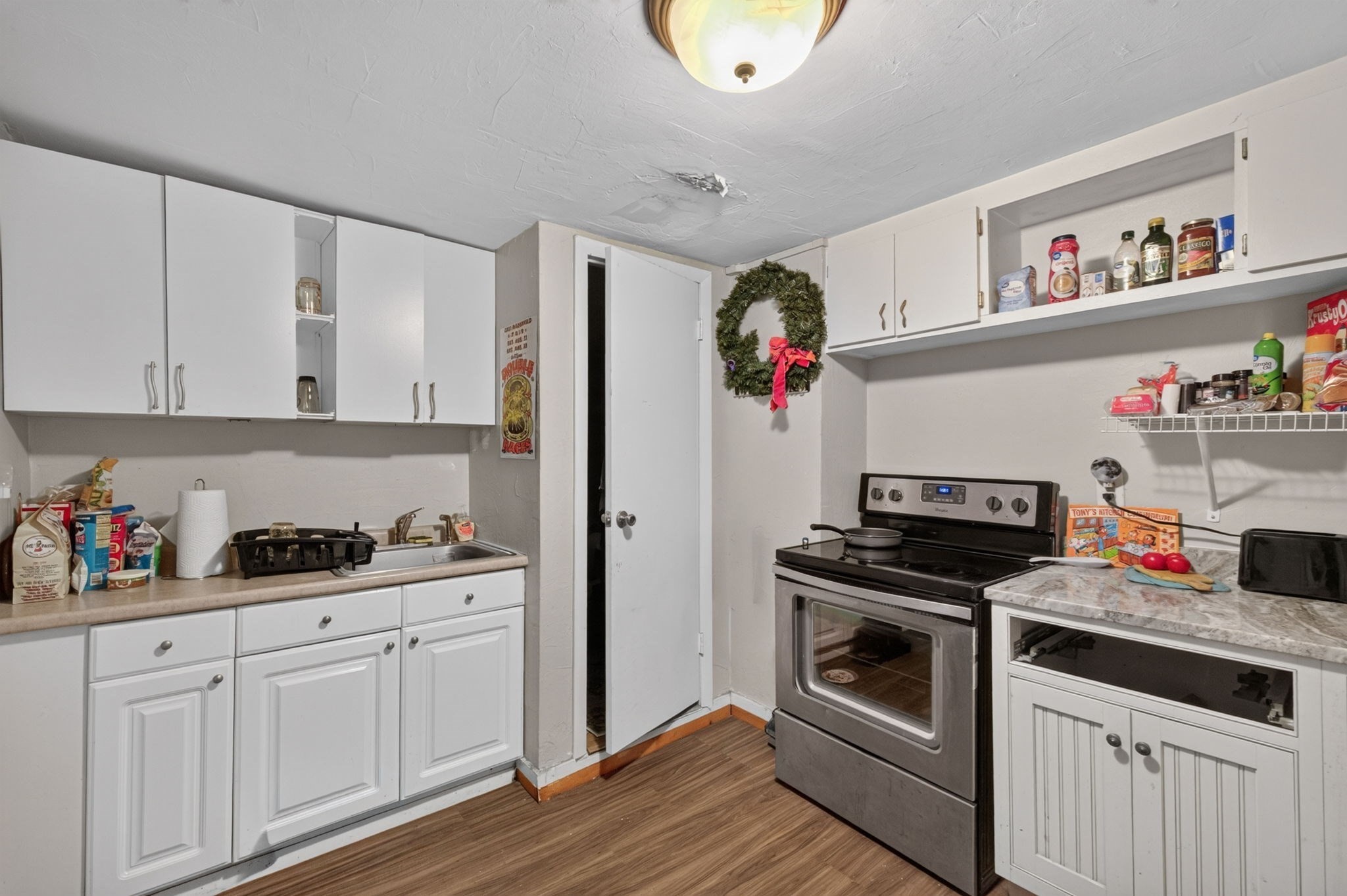 Kitchen with white cabinets, a stainless-steel range, stocked open shelves, and a wreath beside the doorway.