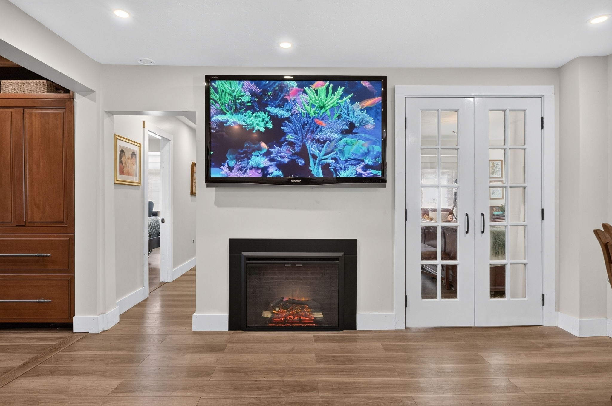 Living room with a fireplace, aquarium display on a wall-mounted TV, glass-paneled French doors, and wood flooring.