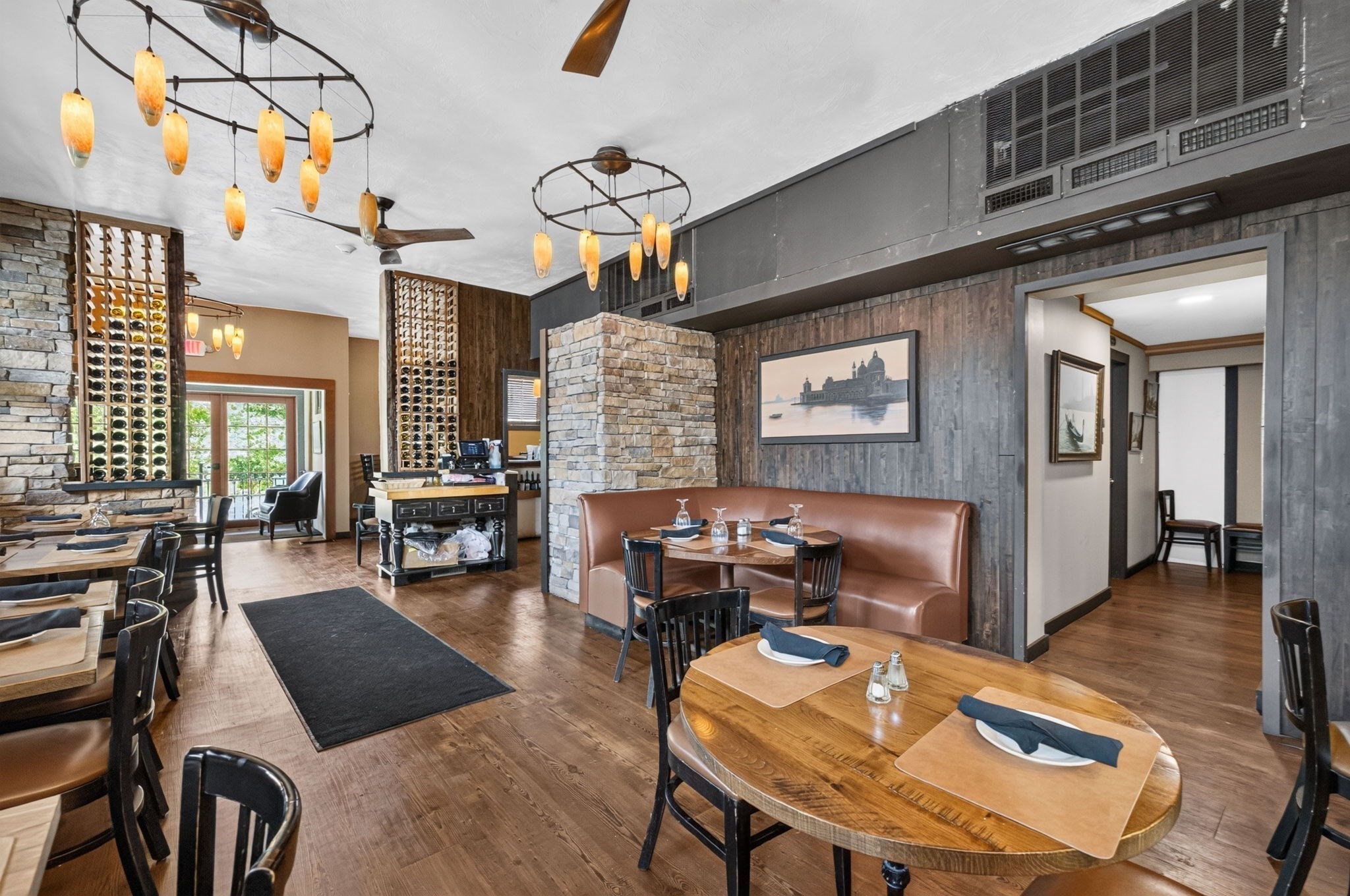 Restaurant dining room with stone partitions, wine racks, and amber pendant lights.