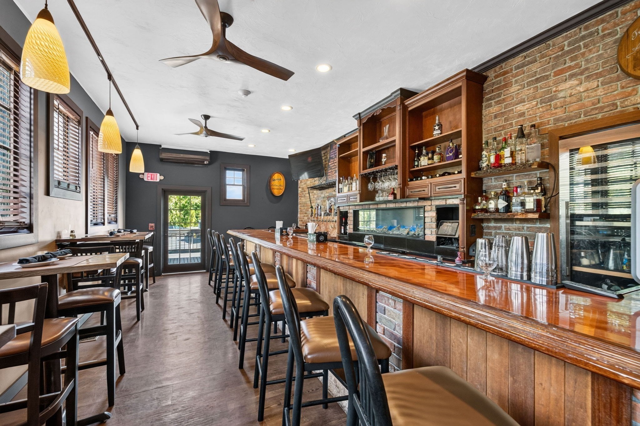 Restaurant bar with a polished wood counter, leather stools, brick walls, and a built-in aquarium.