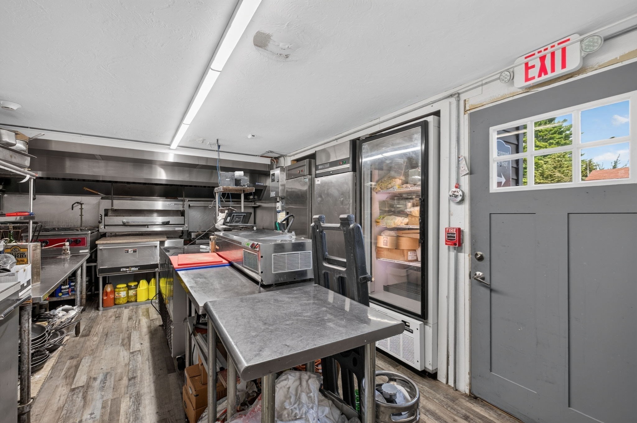 Commercial kitchen with stainless steel prep tables, cooking equipment, and a glass-front refrigerator.