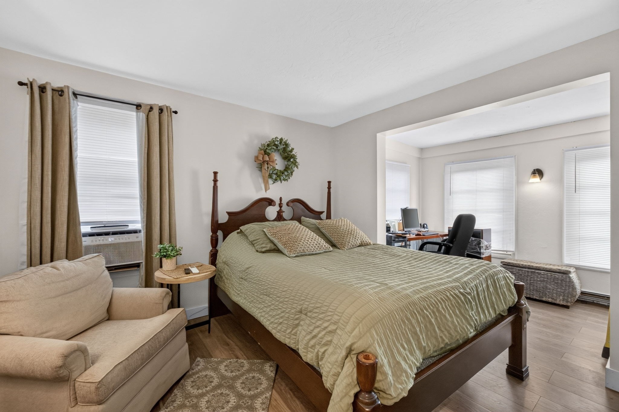 Bedroom with a four-poster bed, beige sofa, and adjoining office nook.