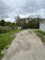 Gravel driveway leading to a fenced entrance, bordered by grass and trees.