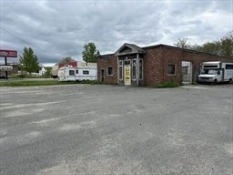 Brick commercial building beside a broad paved parking area under an overcast sky.