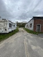 Gravel driveway between a white mobile home and a brick outbuilding.