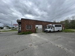 Low brick commercial building beside a cracked asphalt parking area under cloudy skies.