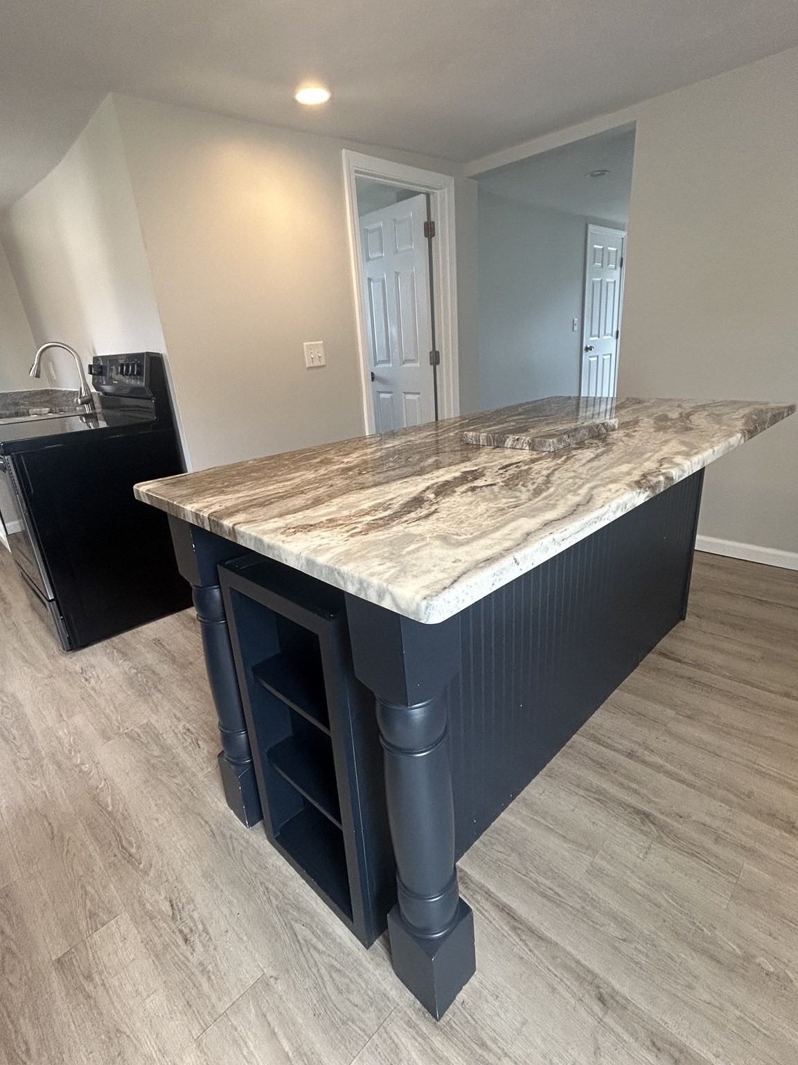 Kitchen with a large veined stone island, dark cabinetry, and gray wood-look flooring.