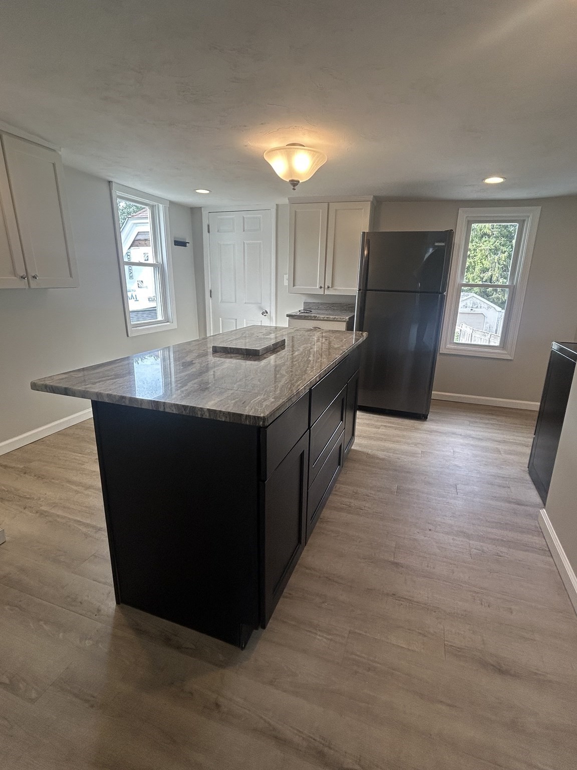Kitchen with a large dark island and stone countertop, light cabinets, and a black refrigerator.