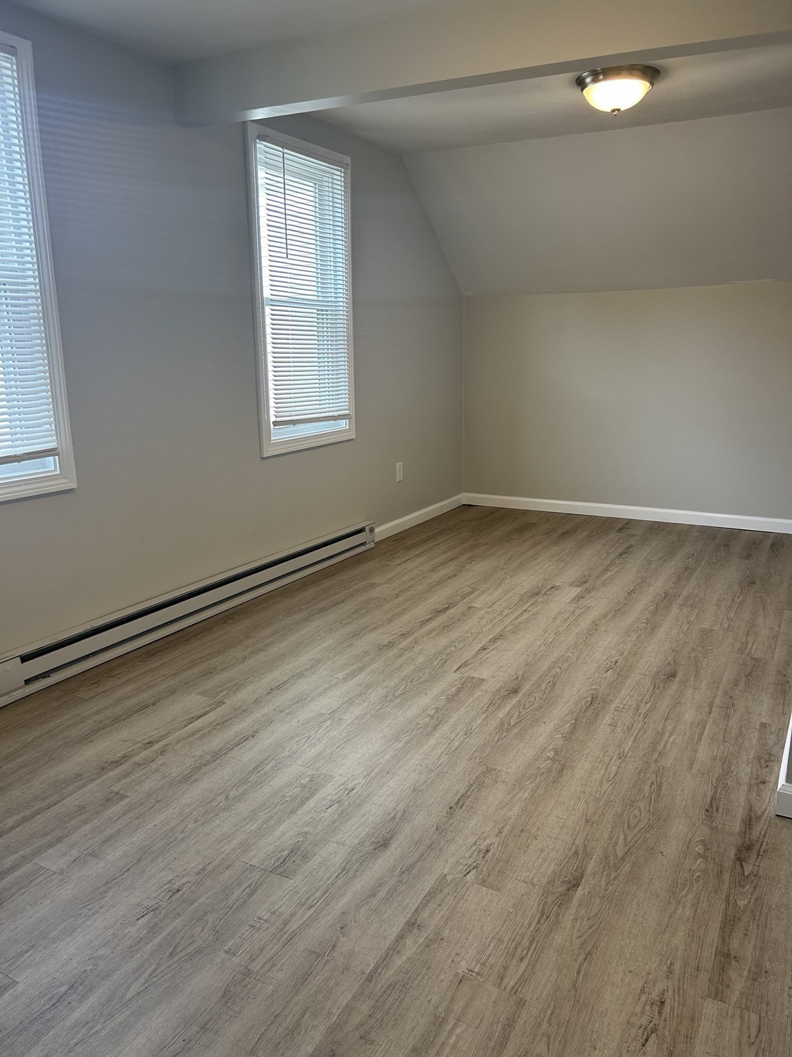 Empty room with wood-look plank flooring, two blinded windows, and a sloped ceiling.
