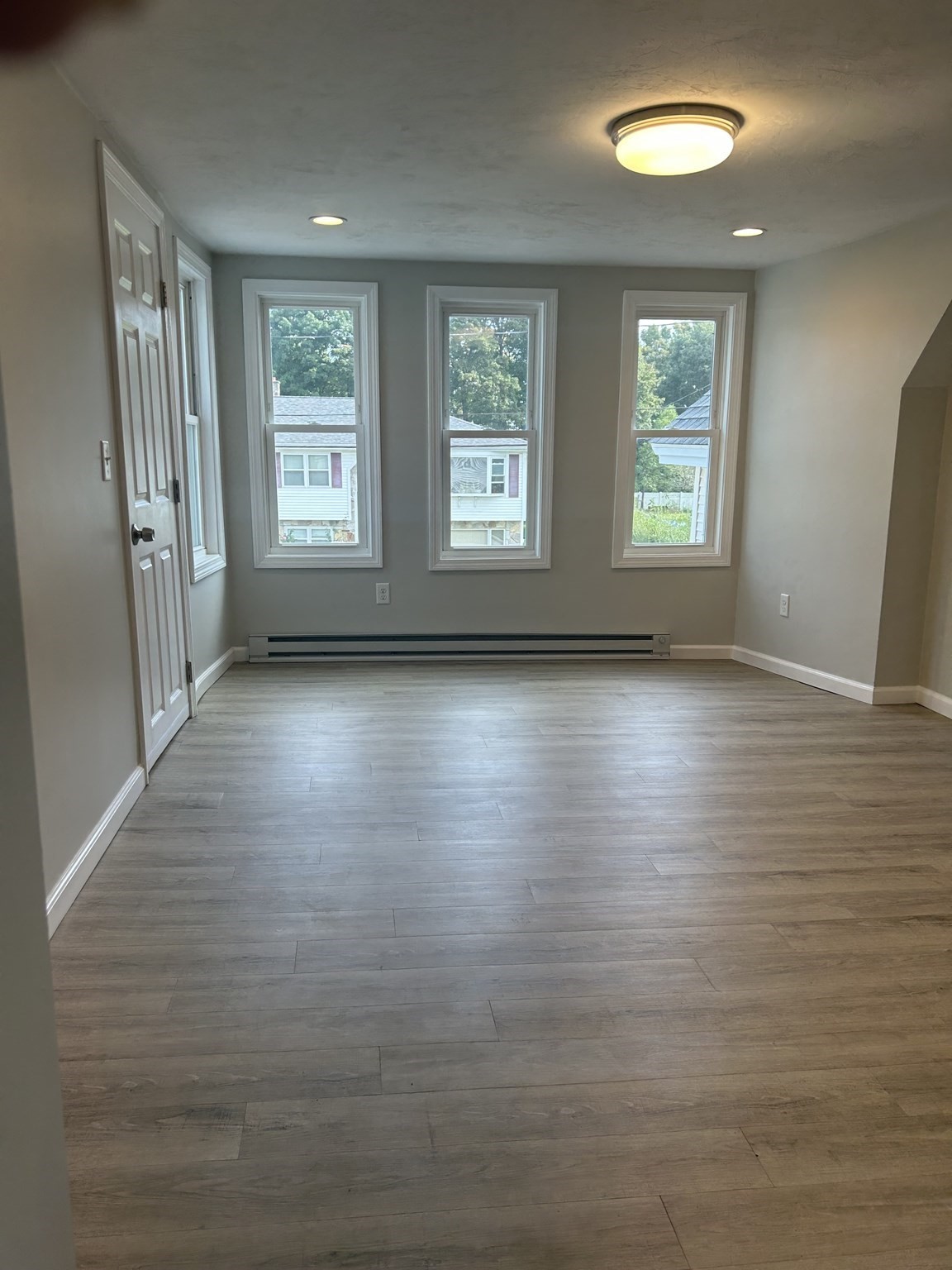 Empty room with gray plank flooring, three tall windows, and a baseboard heater.