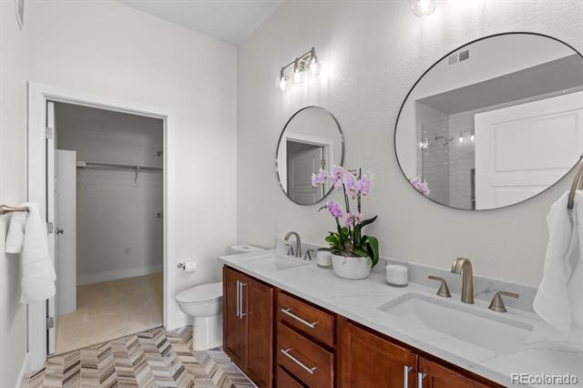 Bathroom with double-sink vanity, round mirrors, purple orchids, and gray-and-white chevron tile floor.