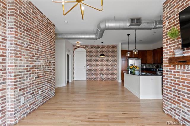 Loft interior with exposed brick walls, light wood floors, and an open kitchen with a white island.
