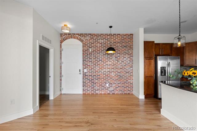 Open dining area with light wood floors, a brick accent wall, and an adjacent kitchen.