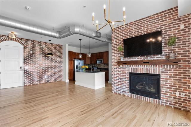 Unfurnished condo living area with exposed brick, hardwood floors, a fireplace, and an open kitchen.