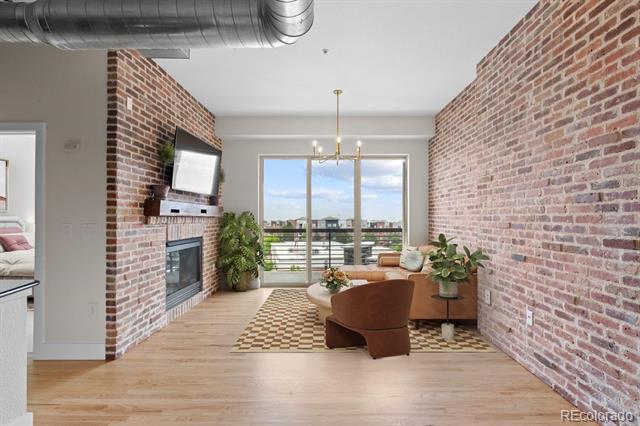 Loft living room with exposed brick walls, fireplace, modern seating, and balcony windows overlooking the city.