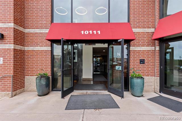 Brick building entrance with glass doors, a red 10111 awning, and teal planters.