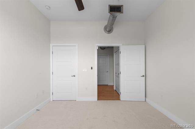 Empty carpeted room with white walls, open doorways, and an exposed ceiling duct.