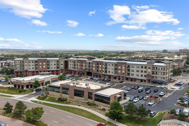 Mixed-use apartment and retail complex with parking lots and roads, viewed from above.