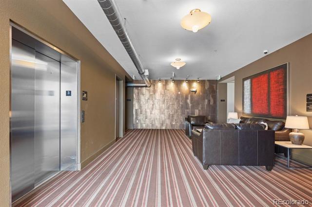 Building lobby with stainless-steel elevator doors, striped carpet, and dark leather seating.